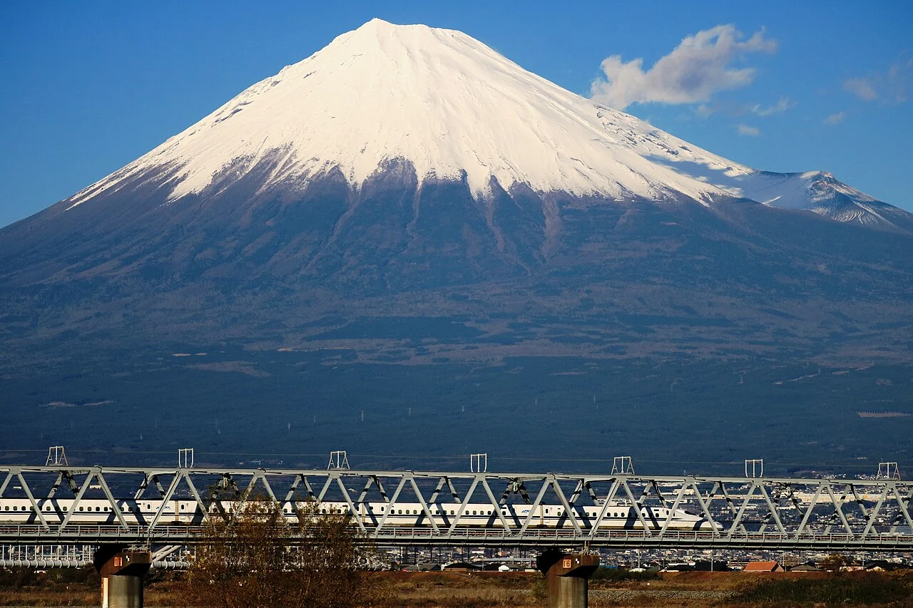 A Shinkansen crosses the Fuji River with Mount Fuji behind it.