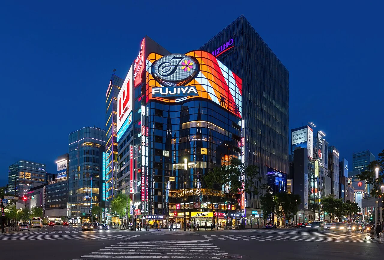 Illuminated shops and signs at a Ginza street corner during blue hour.