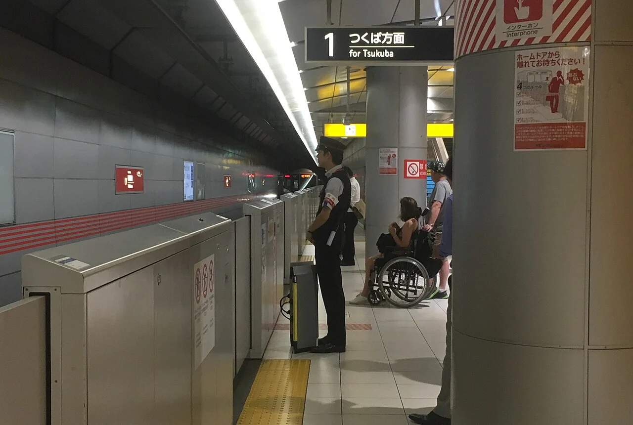 A Tokyo station worker positions an accessibility ramp for a passenger.