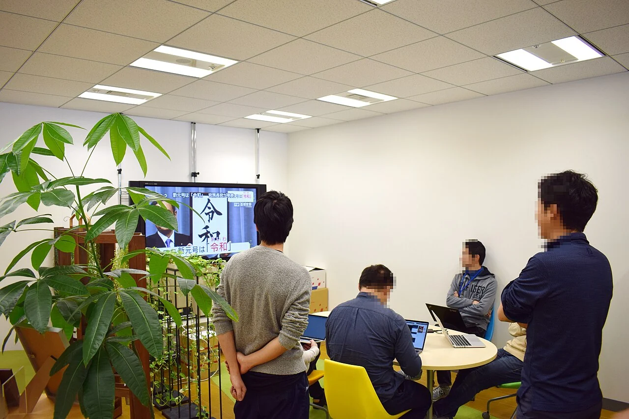 Japanese office colleagues pause together during a television announcement.